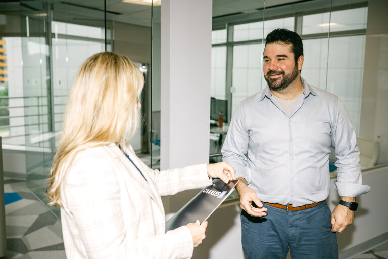 Professional woman giving man folder with Charles IT logo