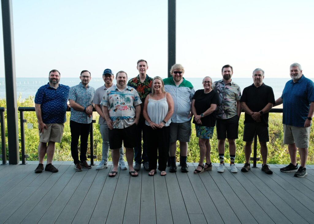 Charles IT Virginia team members gathered outdoors during the company's Beach Day event, standing together on a deck overlooking the water.